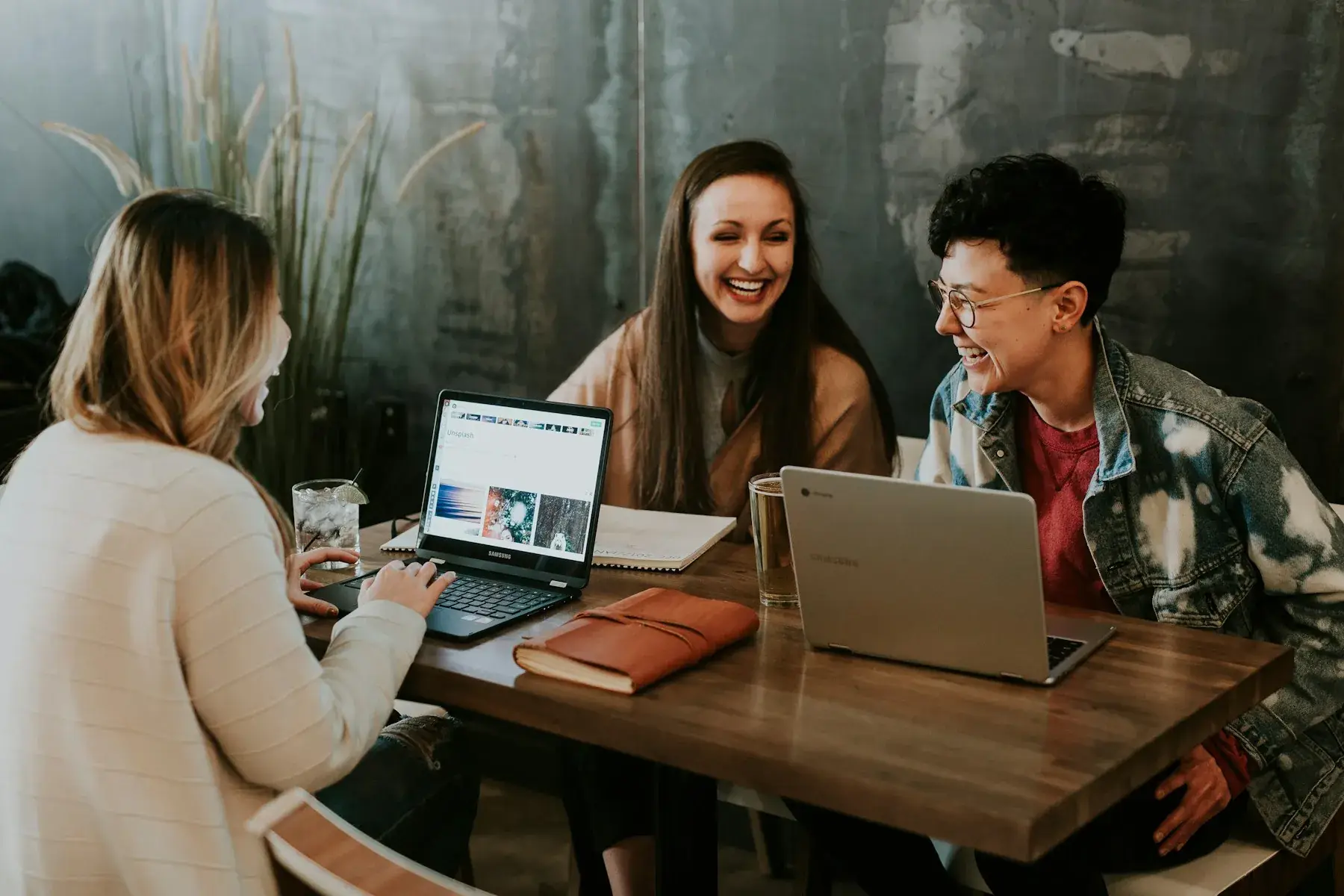 Three colleagues laughing together around a table with laptops