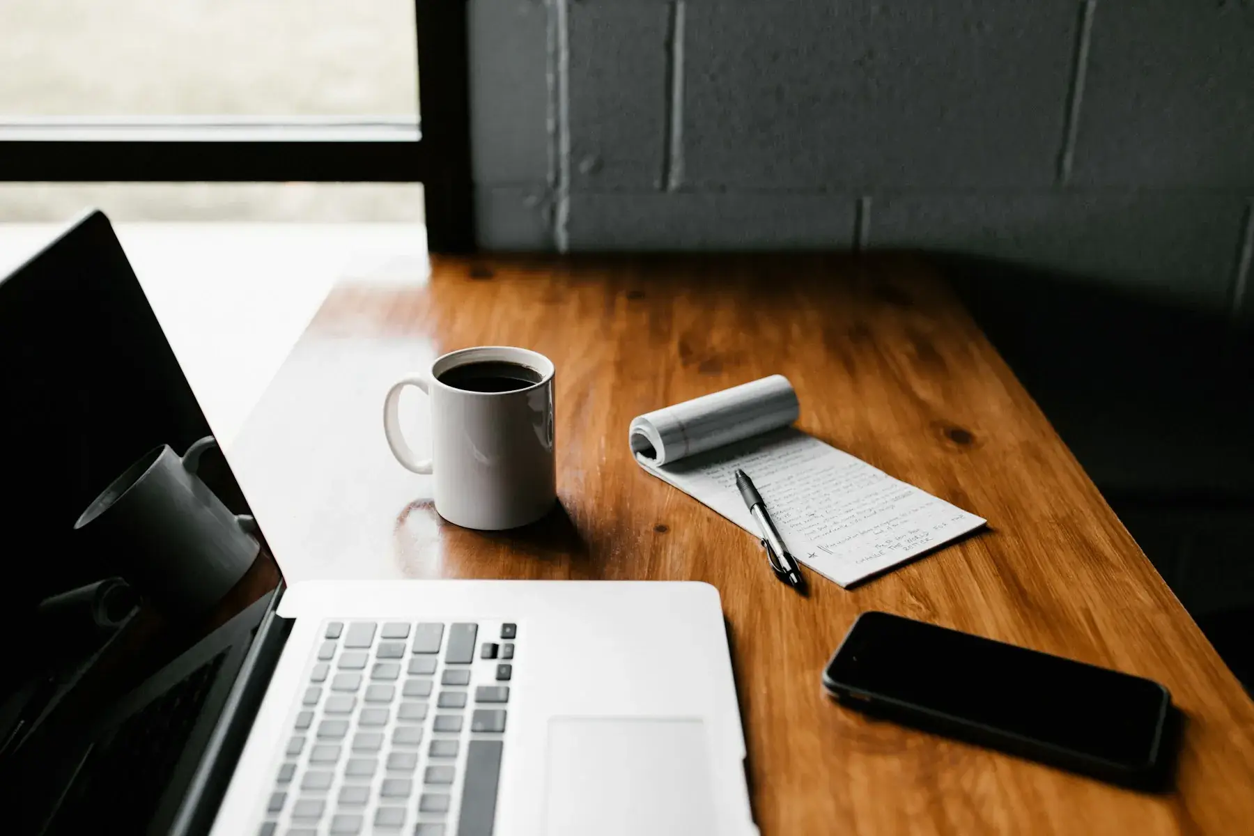 A laptop, coffee mug and phone on a wooden desk
